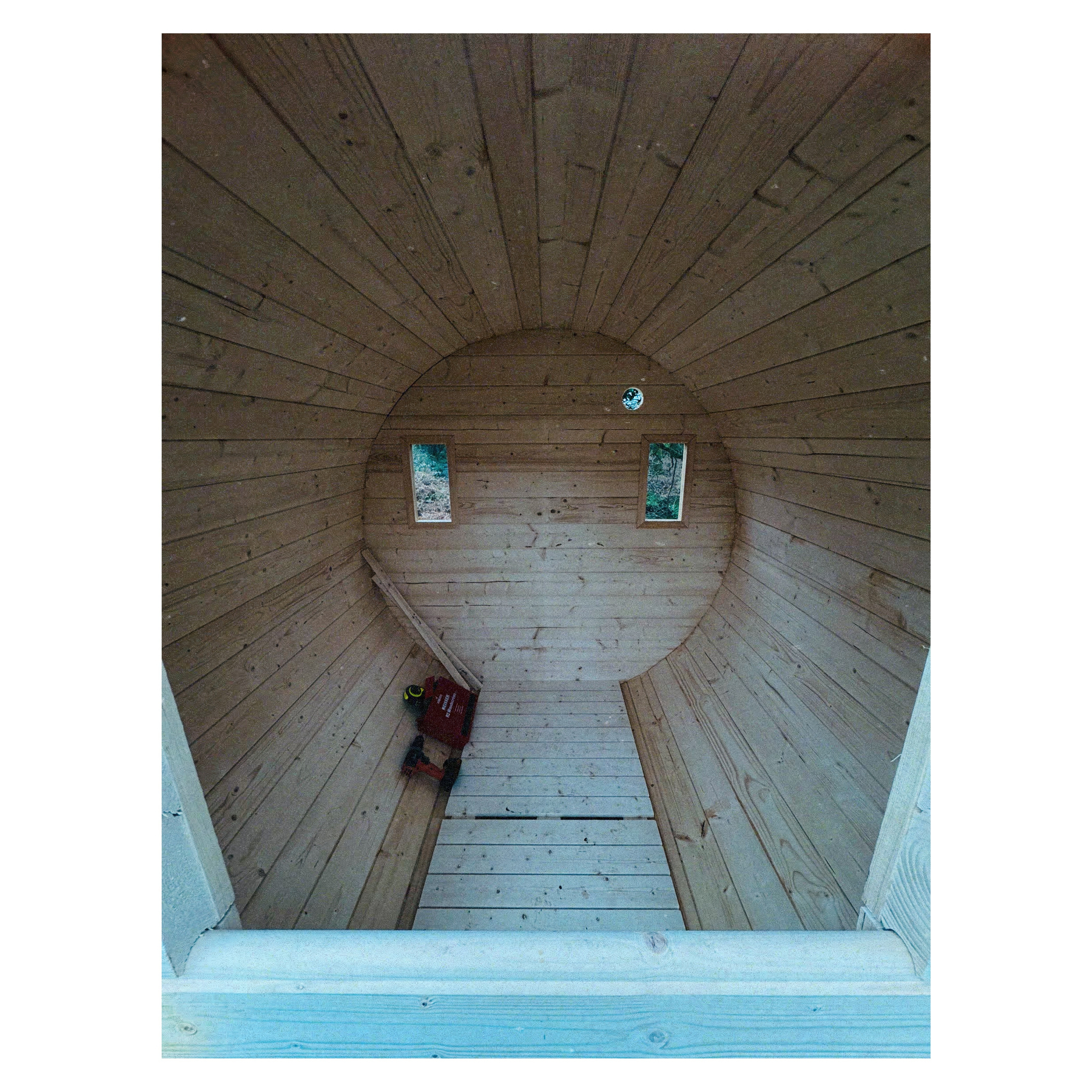 Auto-generated description: A wooden cylindrical structure with two small windows and a bench inside.