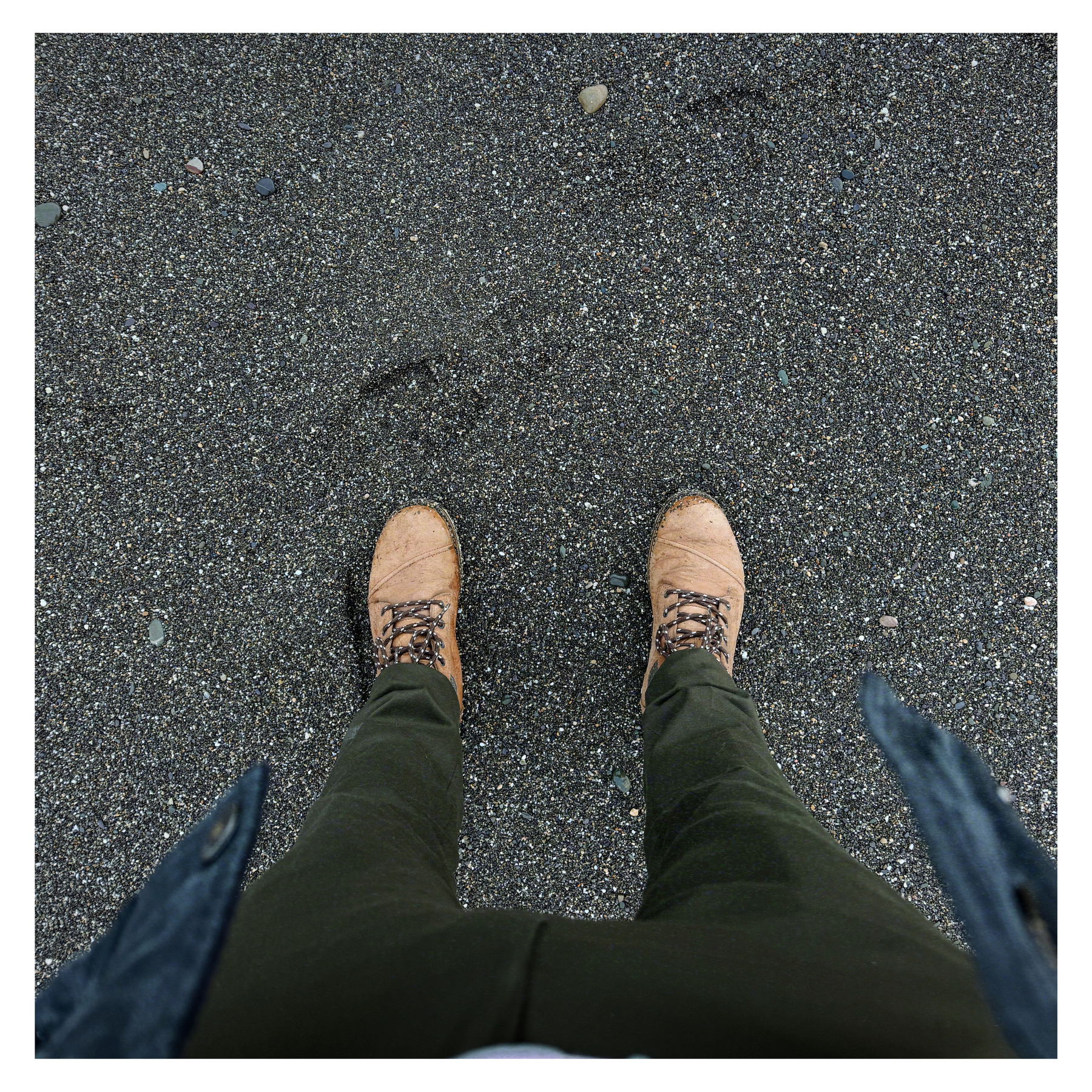 A person is standing on a sandy ground, wearing brown shoes and green pants.