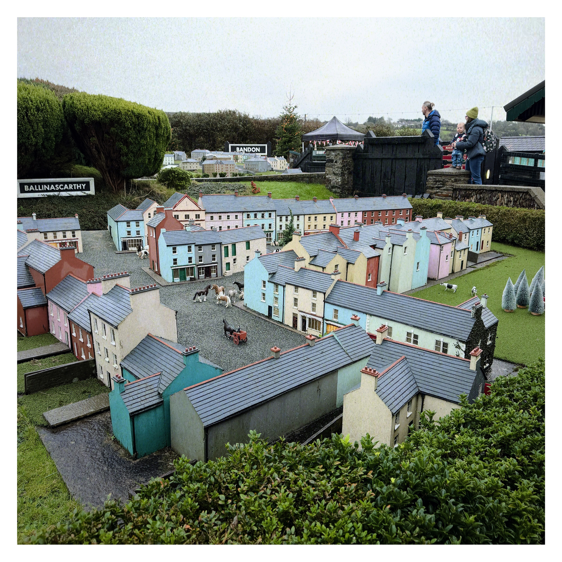 A miniature village with detailed model buildings and streets is observed by two people.