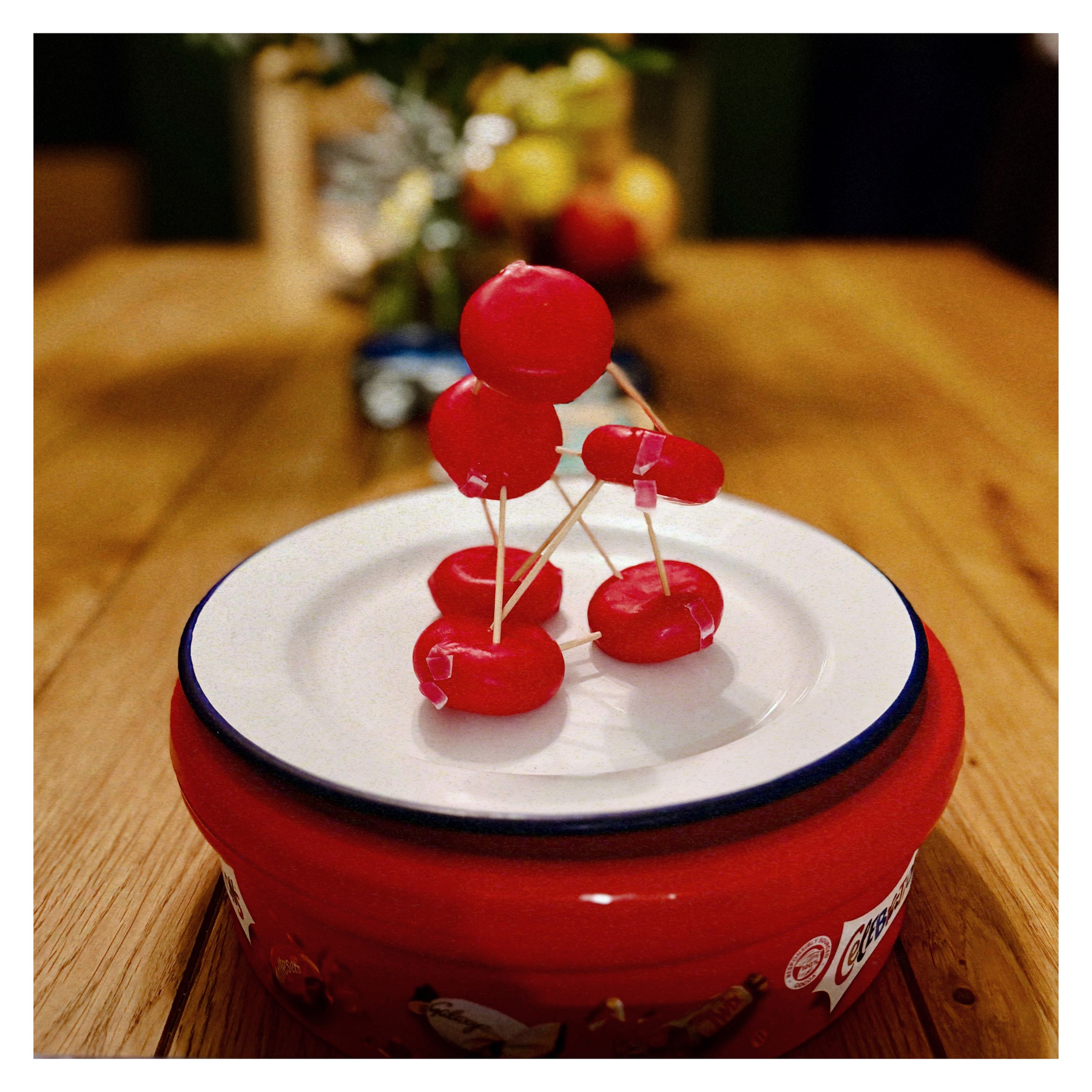 Auto-generated description: Two small figures made of red wax and toothpicks are creatively arranged on a plate.
