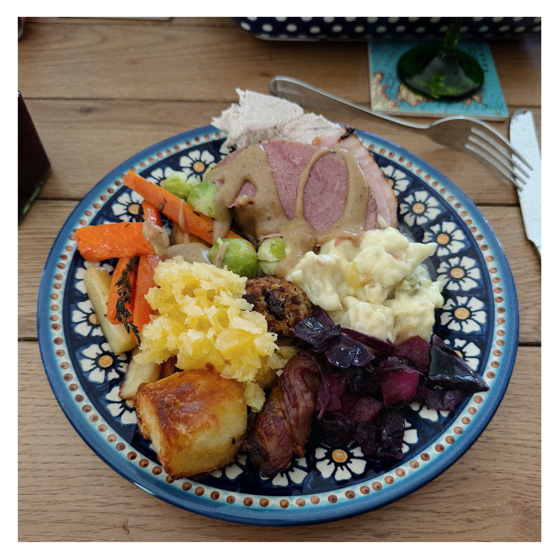 Auto-generated description: A plate filled with a variety of foods, including roasted meats, vegetables, potatoes, and a creamy sauce.