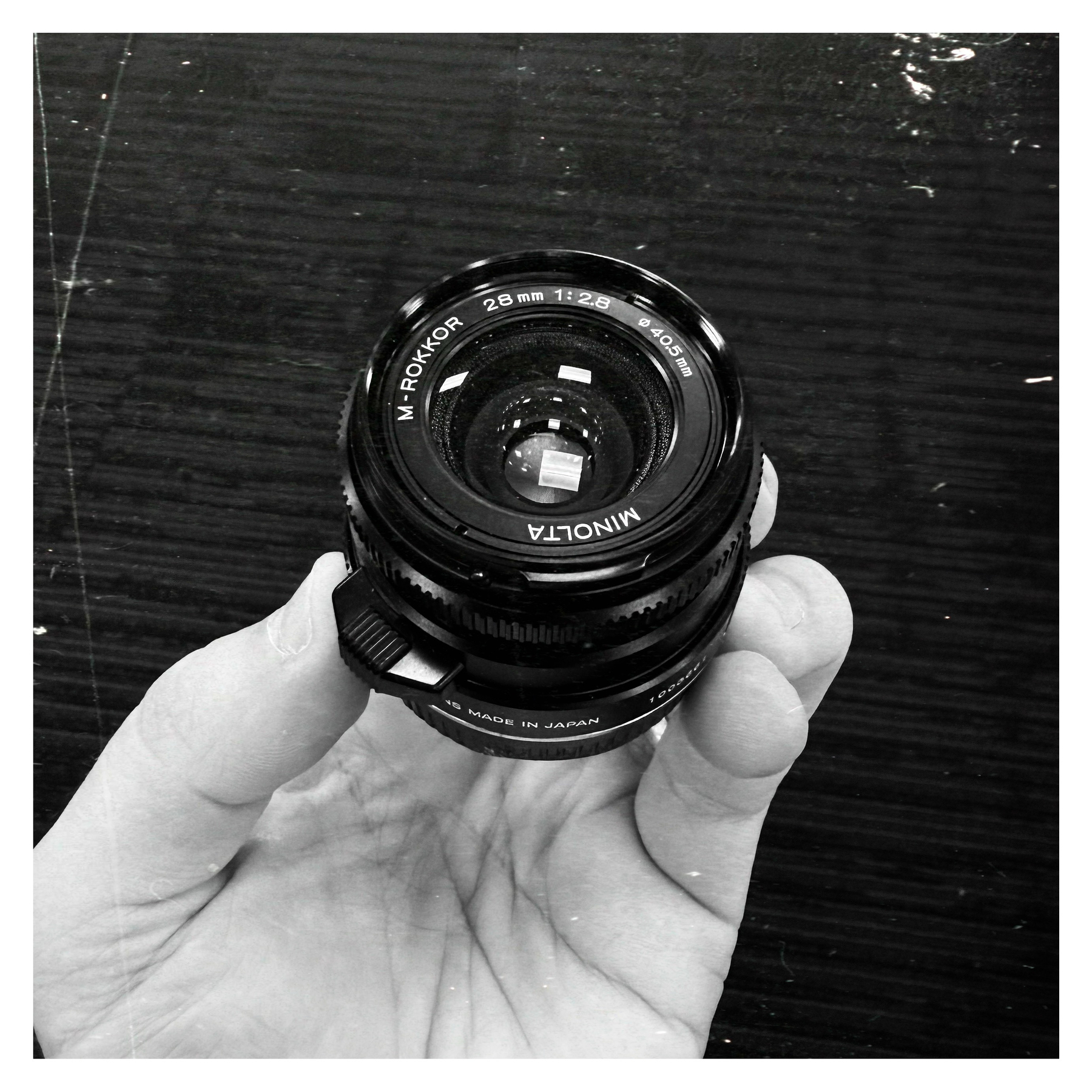 Auto-generated description: A hand is holding a Minolta M-Rokkor 28mm camera lens.